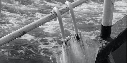 schwarz-weiss Bild von zwei Regenschirmen mit Meer im Hintergrund
